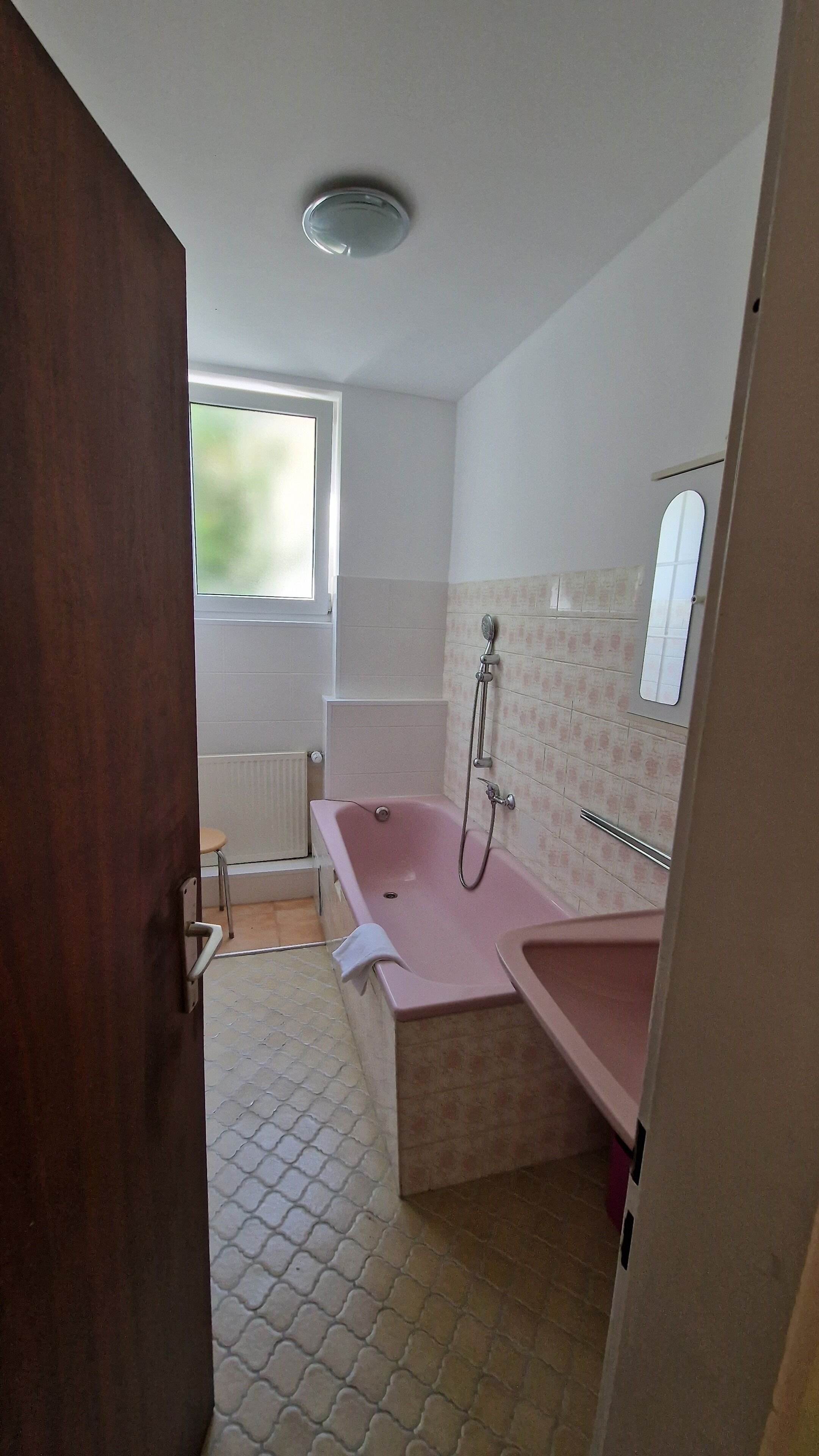 A bathroom with a pink bathtub, a window, and a tiled floor.