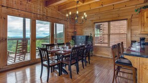 Interior d'una cabana de fusta amb menjador, cuina i finestres grans que ofereixen vistes panoràmiques.