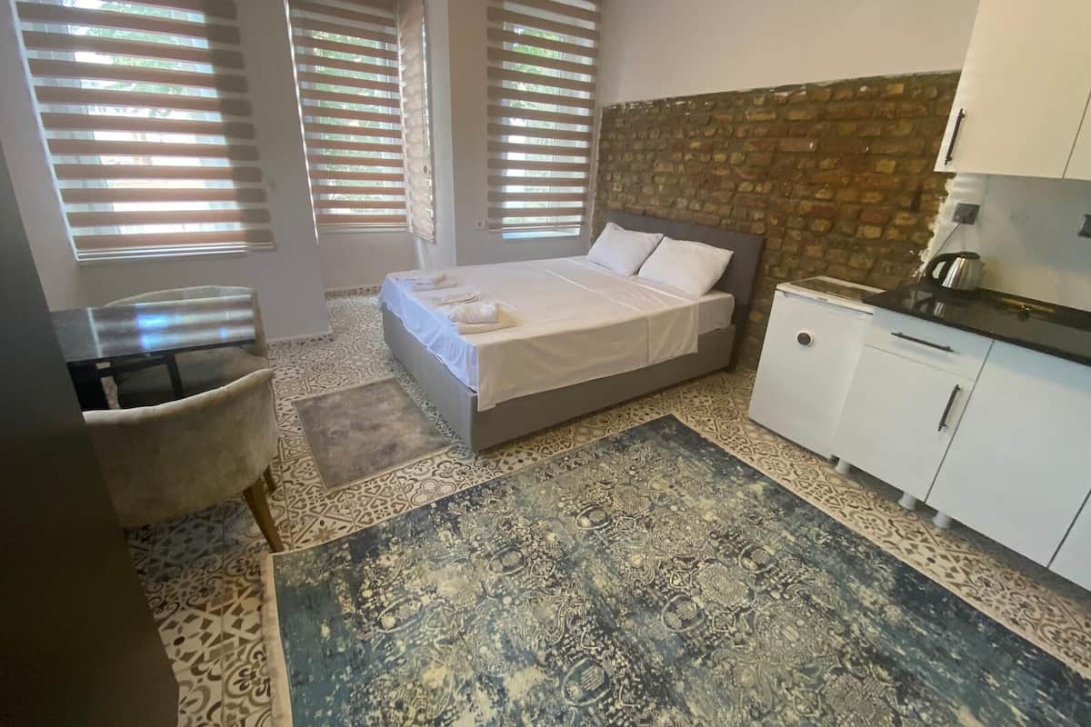 A bedroom with a bed, a desk, a chair, and a kitchenette.