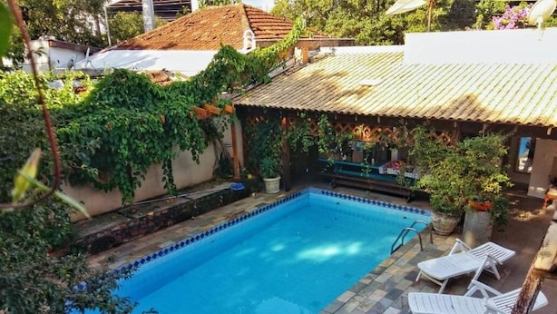 A rectangular swimming pool with a tiled edge, surrounded by a patio area with white lounge chairs. - ALPHA HOSPEDARIA (Londrina)