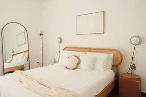 Un letto rifatto con cura, una testiera in legno, un comodino con una lampada e un quadro appeso alla parete.
