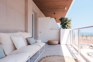 Un balcone moderno con un divano bianco, un poggiapiedi rotondo e vista sul mare.