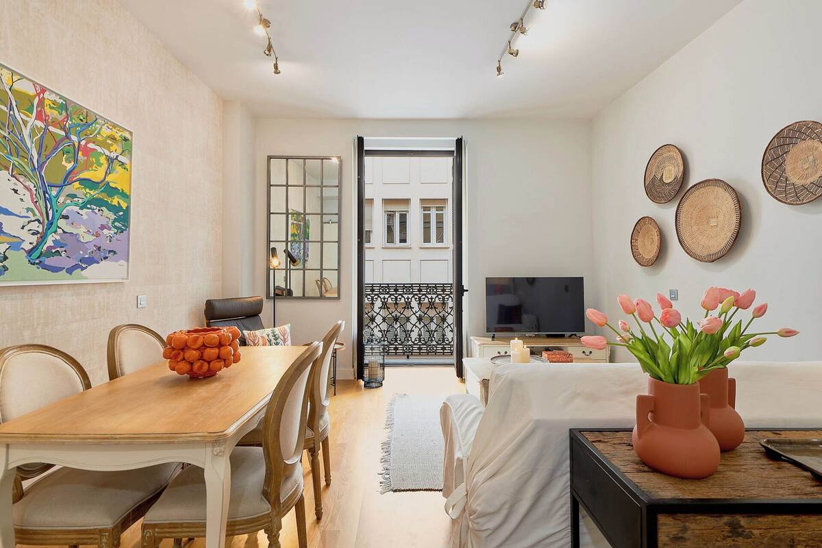 A dining area with a wooden table and chairs, a vase of flowers, and a television in the background.