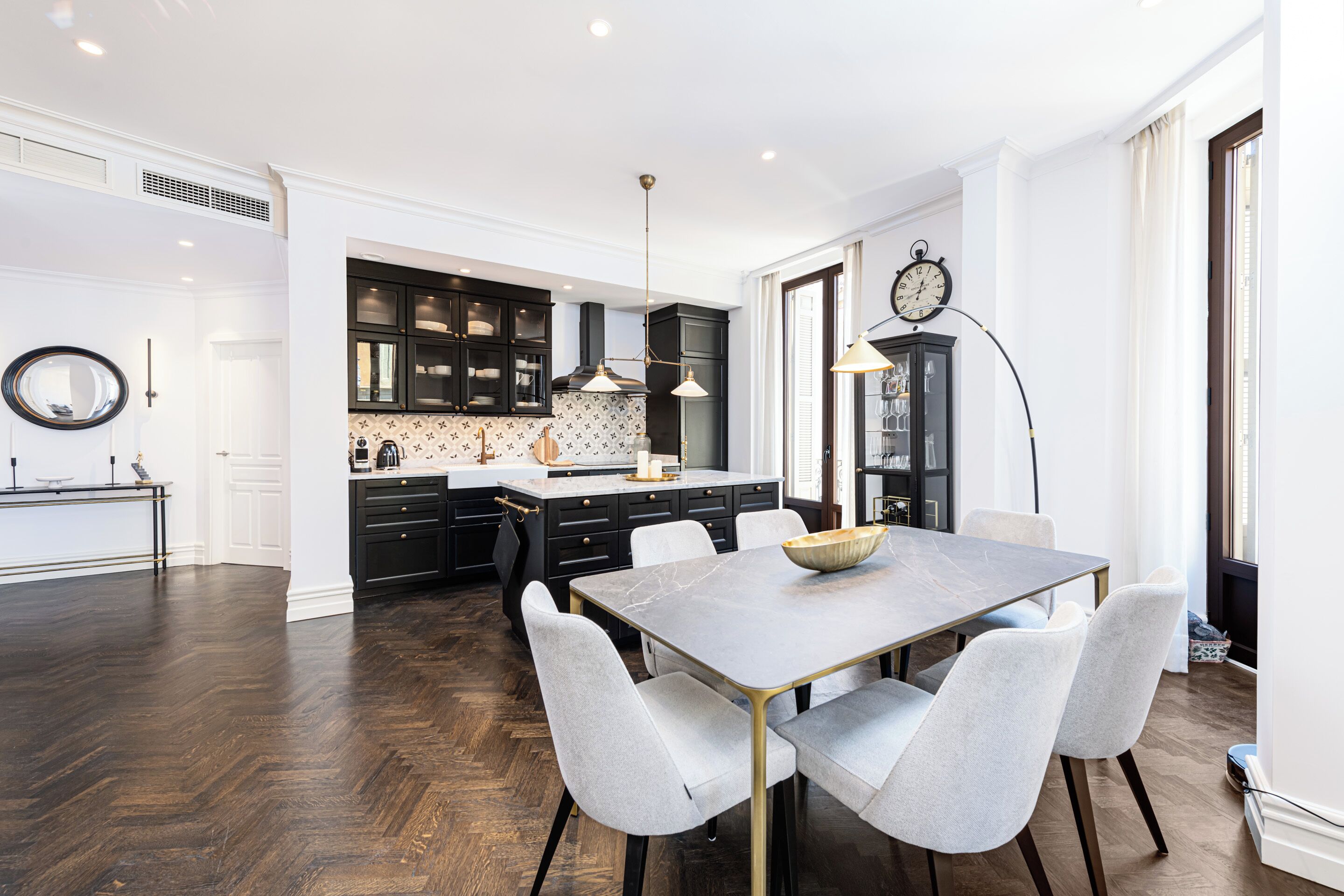 A modern kitchen with dark wood flooring, a marble dining table, and light grey upholstered chairs.
