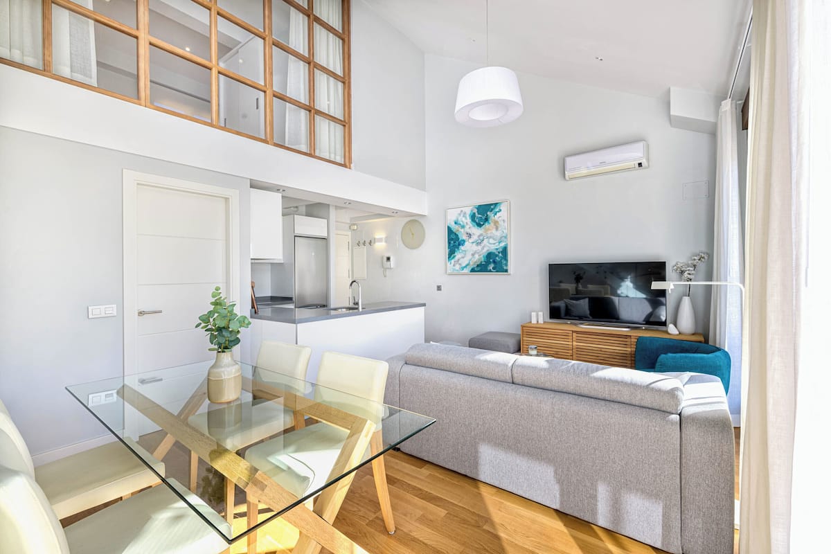 A modern apartment with a glass dining table, grey sofa, and a TV in the living area.