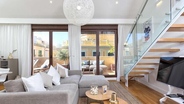 A modern living room with a grey sofa, a glass staircase, and a large TV. - Solaga Souviron Suits (Málaga)