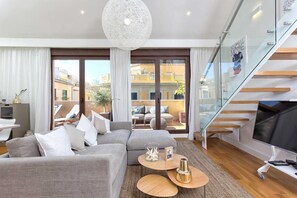 Un soggiorno moderno con un divano grigio, una scala in vetro e un grande televisore.