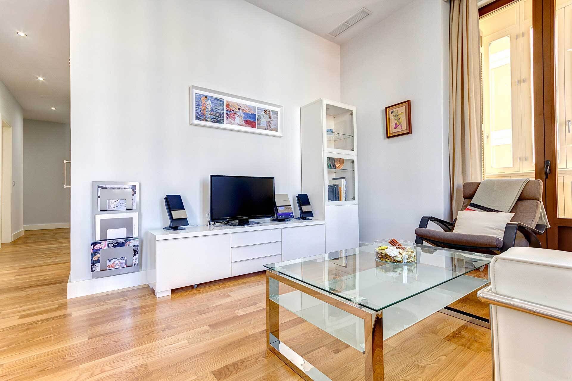 Un salon moderne avec une table basse en verre, un meuble de rangement pour appareils multimédias blanc et un coin salon confortable.