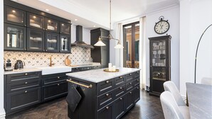 A modern kitchen with dark cabinetry, a marble island, and a clock on the wall. - Solaga Souviron Suits (Málaga)