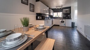 A modern kitchen with dark flooring, white cabinetry, and a dining area set with plates and cutlery. - Spacious 3 Bed House, 5mins to HS2/ NEC/Airport. (Birmingham)