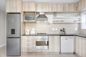 Una cocina moderna con alacenas de madera clara, electrodomésticos de acero inoxidable y una encimera negra.