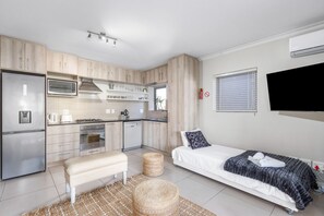 Una cocina compacta con electrodomésticos modernos, un banco y una cama con cobija.