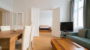 Ein modernes Hotelzimmer mit einem Holztisch, einer Couch, einem Fernseher und einem großen Fenster mit Vorhängen.