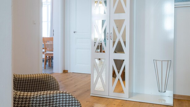 Ein Zimmer mit einem stuhlbezogenen Sessel mit Hundepunktmuster, einem weißen Schrank mit verzierten Ausschnitten und Holzboden.