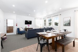 A modern living room with a sofa, a dining table set for four, and a TV mounted on the wall.
