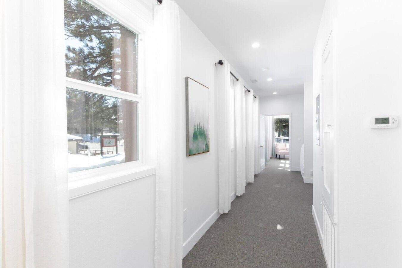 A hallway with white walls, a grey carpet, and a framed picture on the wall.