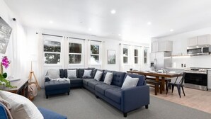 A modern living room with a sectional sofa, a dining table, and a kitchen area with white cabinets and stainless steel appliances. - #9 New! 3 bedroom Apartment in Town (Mammoth Lakes)