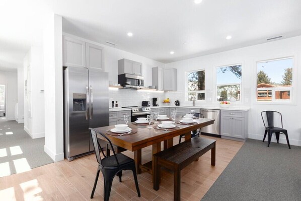 A modern kitchen with white cabinets, stainless steel appliances, and a dining area with a wooden table and chairs.