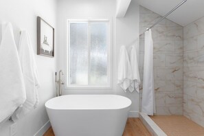 Ein modernes Badezimmer mit einer freistehenden Badewanne, einer Dusche mit Glastür und einem großen Fenster.
