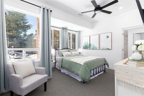 A bedroom with a bed, a chair, a bedside table, a lamp, and artwork on the wall.