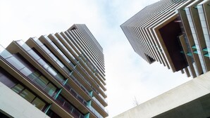 Dos edificios de gran altura con un diseño arquitectónico moderno, que incluyen varios balcones y un cielo despejado al fondo.