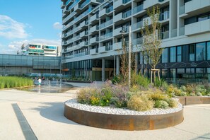 Un bâtiment moderne doté de nombreux balcons et d’un espace paysager agrémenté de plantes et d’un élément décoratif aquatique.