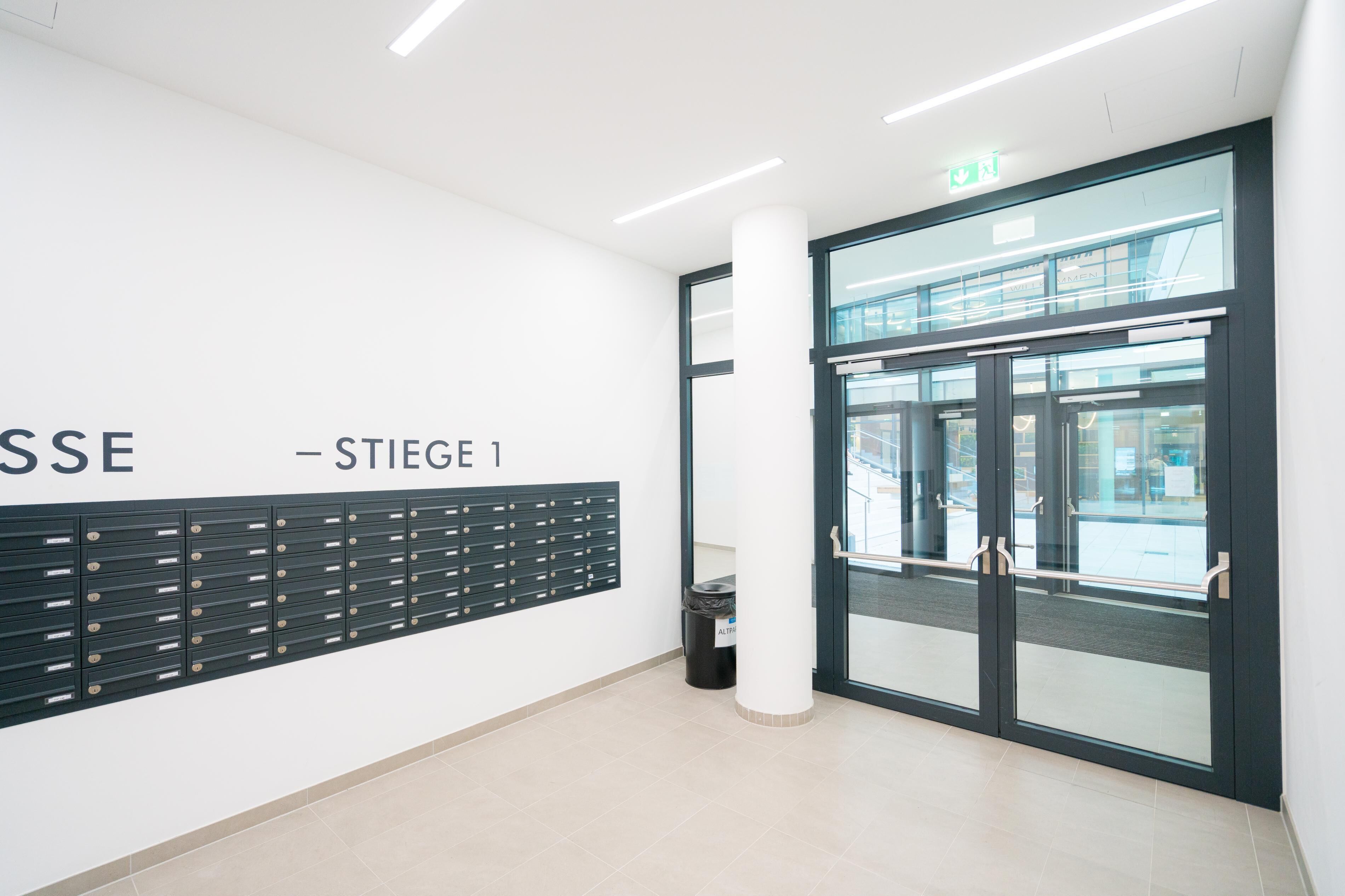 A modern interior with a wall-mounted storage unit, a glass door entrance, and a clean, tiled floor.