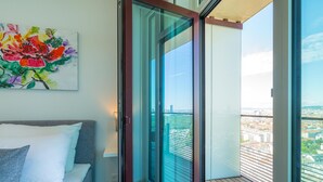 Un dormitorio con cama, un cuadro y balcón con vista a la ciudad.