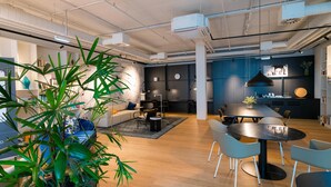 Un espacio de oficina moderno con una mesa redonda, sillas, un sofá y una planta grande en maceta.