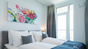 Una habitación de hotel con cama, almohadas, un cuadro, una ventana y cortinas.