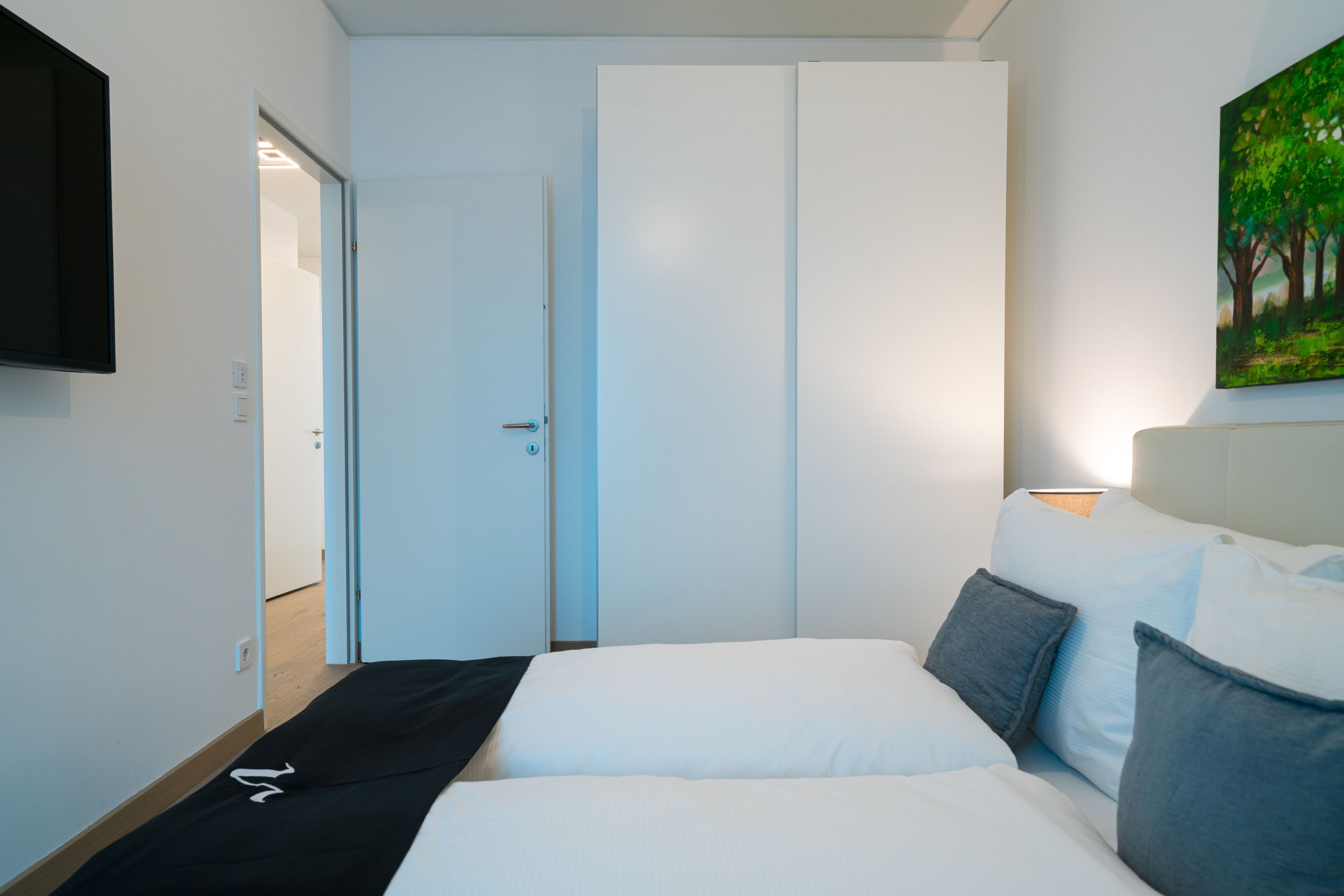 Ein modernes Hotelzimmer mit einem Bett, einem Wand-Fernseher und einem Baumgemälde.