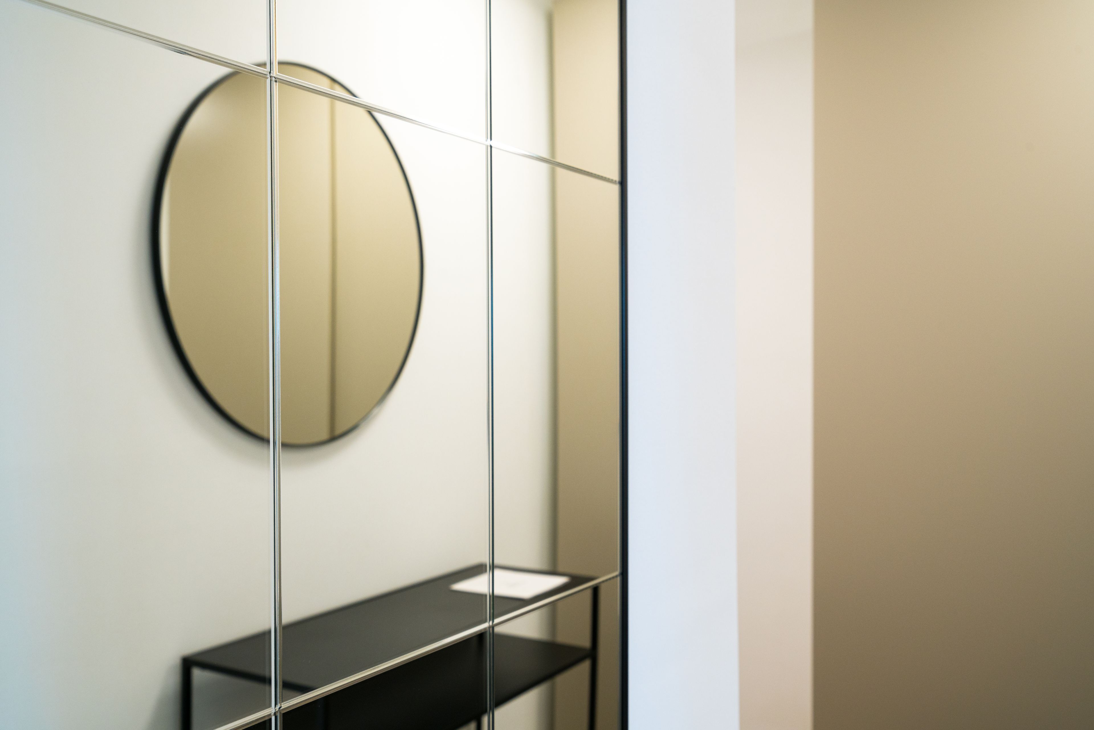 A modern bathroom with a round mirror, a black shelf, and a glass partition.