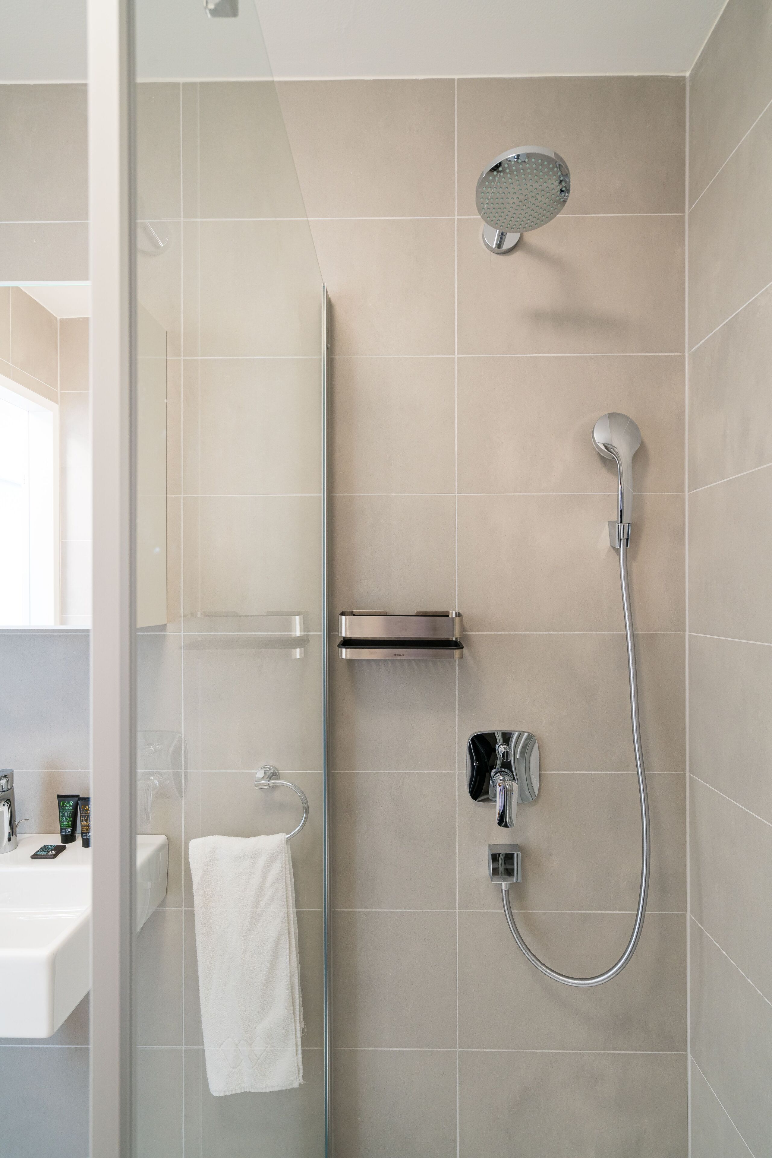 A modern bathroom with a glass shower enclosure, a handheld showerhead, a wall-mounted faucet, and a towel rack.