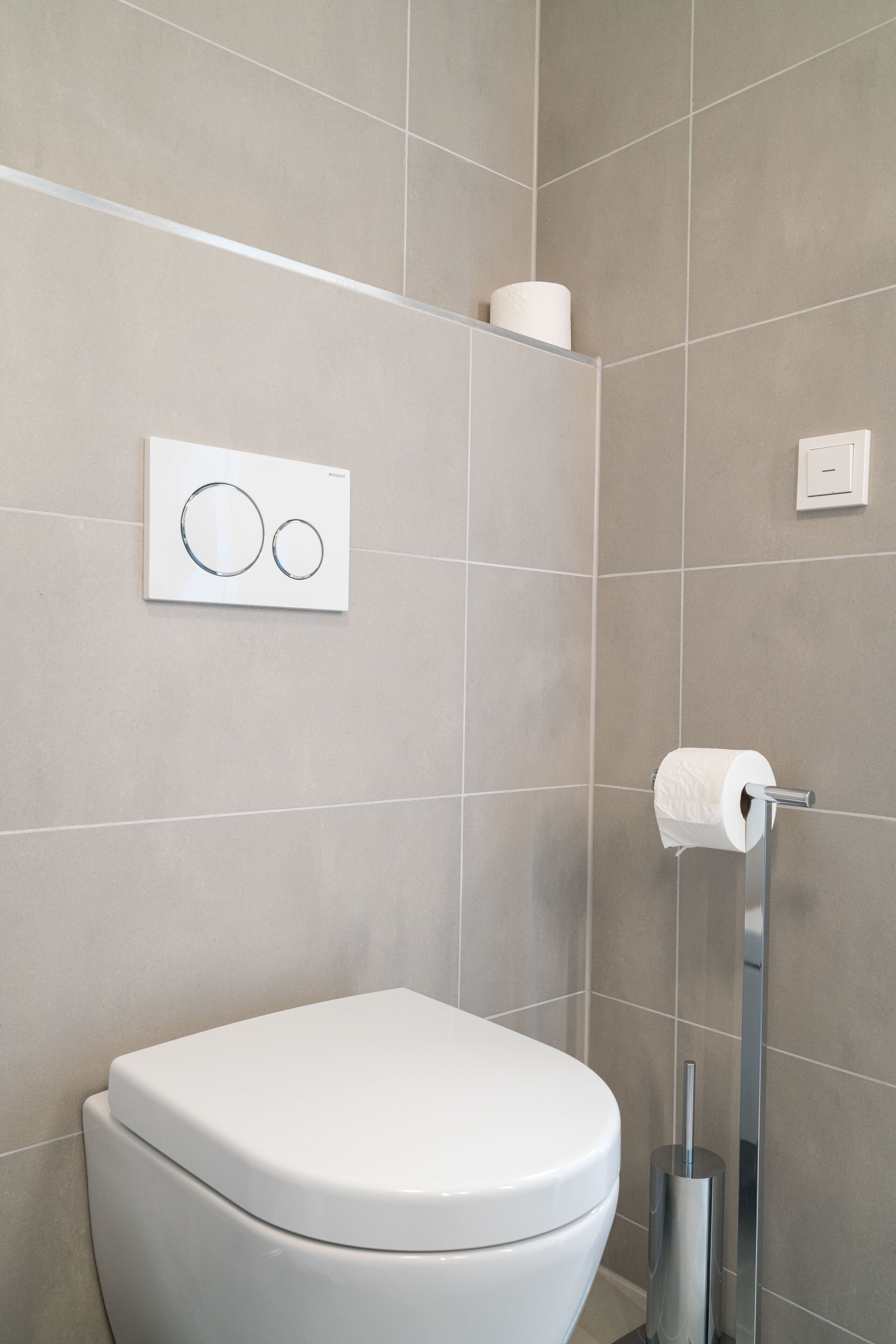 Ein modernes Badezimmer mit Toilette, Toilettenpapierhalter und Wandspender für Toilettenpapier.