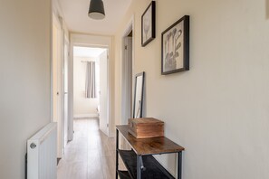 A hallway with a radiator, a table with a box, and framed pictures on the wall.