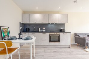 A modern kitchen with grey cabinets, a built-in oven, and a dining area with a white table and chairs. - Hamilton Hideaway | St Andrews (St Andrews)