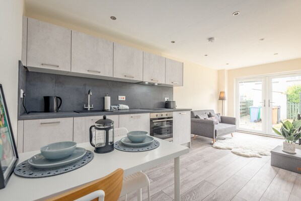 A modern kitchen with grey cabinets, a white countertop, and a dining area with a table and chairs.