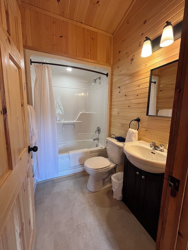 Une salle de bain aux murs lambrissés, équipée d’une douche, de toilettes et d’un lavabo.