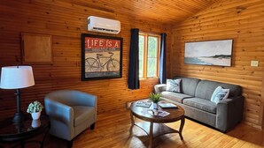 L’intérieur d’un chalet accueillant, avec un plafond en bois, un canapé, un fauteuil, une table basse et un tableau encadré au mur.