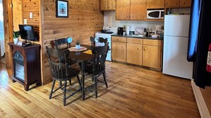 Une cuisine chaleureuse, aménagée dans le style d’un chalet, avec des murs et des planchers en bois, un coin repas avec une table et des chaises, et les appareils de cuisine de base.