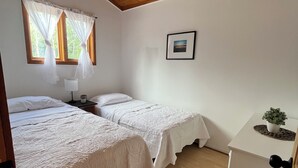 Une chambre avec deux lits, une petite table sur laquelle est posée une plante, un tableau accroché au mur et une fenêtre avec des rideaux.