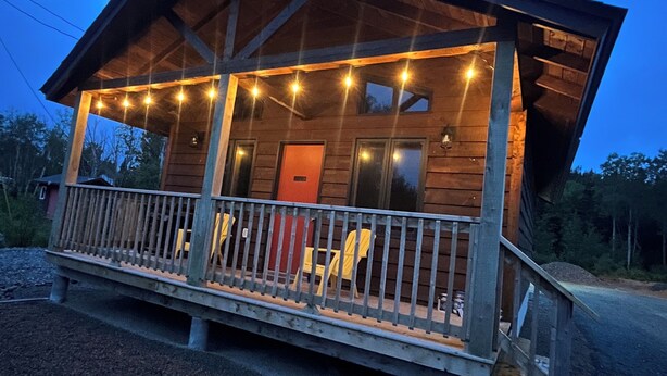 Une cabane en bois avec une véranda, une porte rouge et des guirlandes lumineuses.