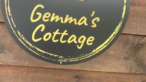 Een rond bord met de tekst “Gemma's Cottage” en een eenvoudig icoontje van een huis, een boom en de zon.