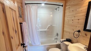 Een kleine badkamer met houten lambrisering, voorzien van een bad, toilet en wastafel.