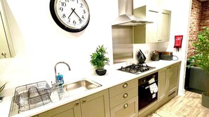 A kitchen with a sink, stove, cabinets, and a clock on the wall.