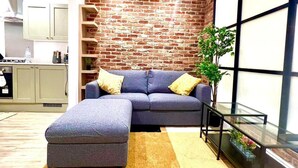 A living room with a grey sectional sofa, a glass coffee table, and a brick wall.