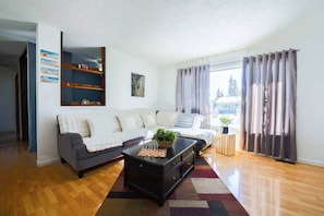 A living room with a sofa, a coffee table, a chessboard, and a window with curtains.