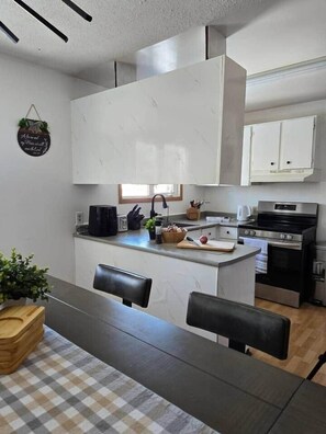 A modern kitchen with white cabinets, a central island, and a dining area with a checkered tablecloth.