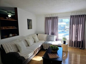 A living room with a sofa, a coffee table with a plant, and a window with curtains.