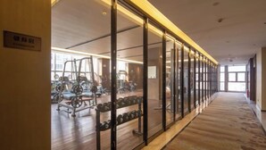 A gym with exercise equipment, a wooden floor, and large windows. - Jing Jiang Hotel (Lianjiang)